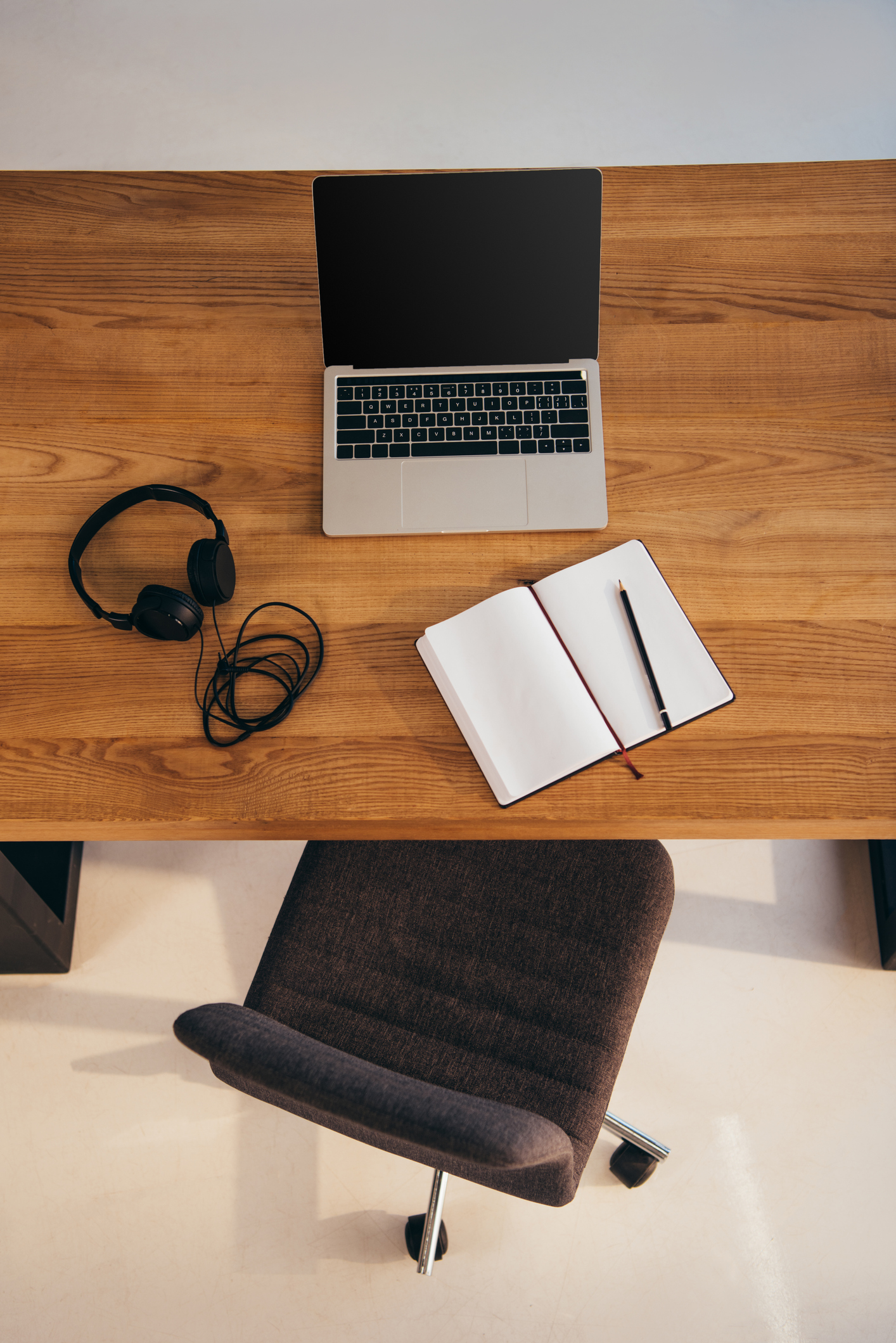 top view of laptop with blank screen, headphones and notebook on wooden table with office chair near by